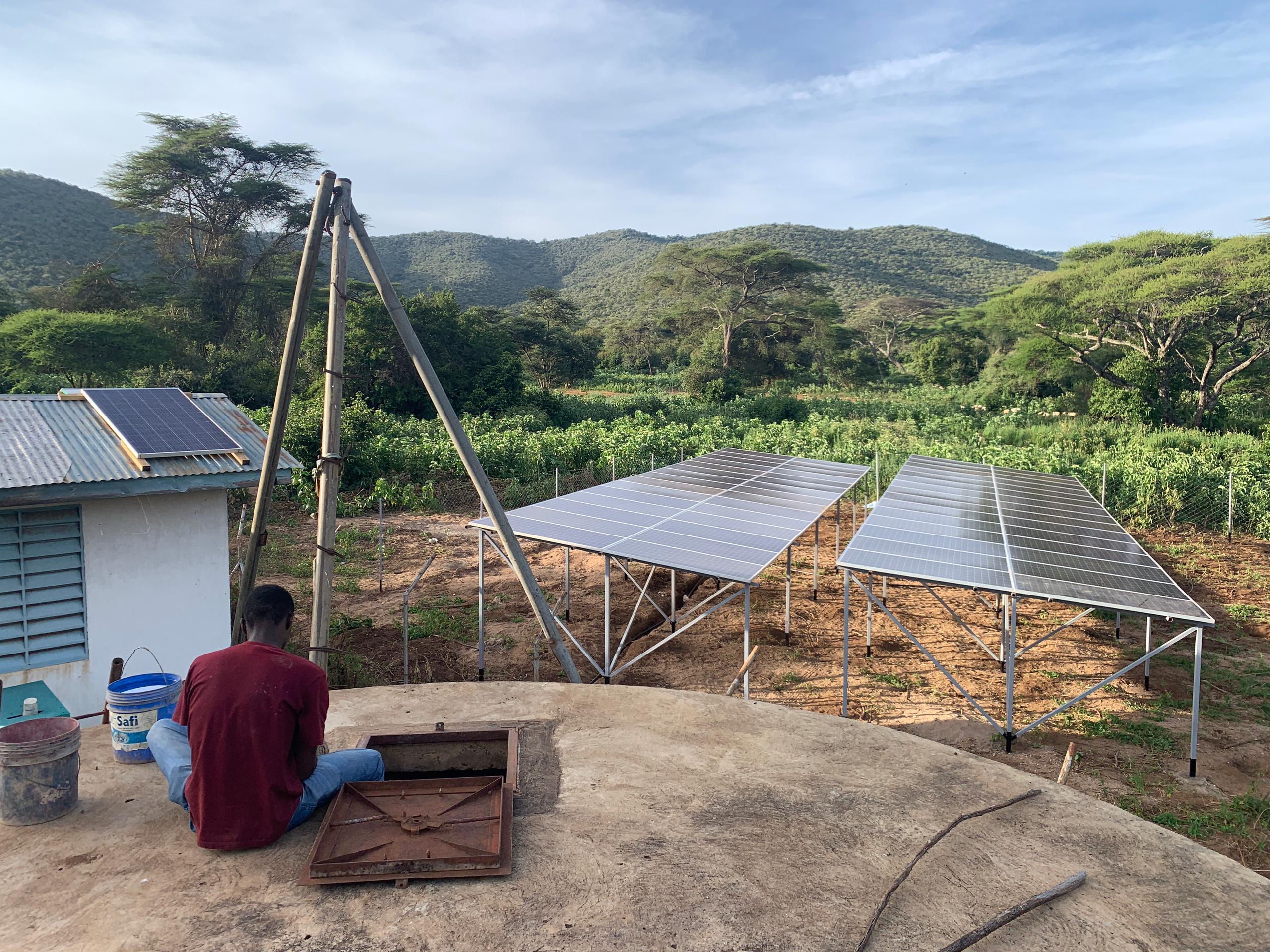 A person sitting on a large storage tank with a newly installed water solar system infront.